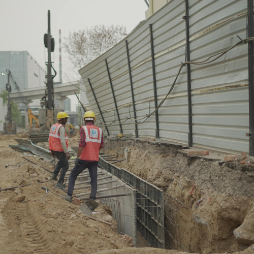 Construction workers building a diaphragm wall at a construction site in Gurgaon, with machinery in the background and safety barriers alongside the excavation.